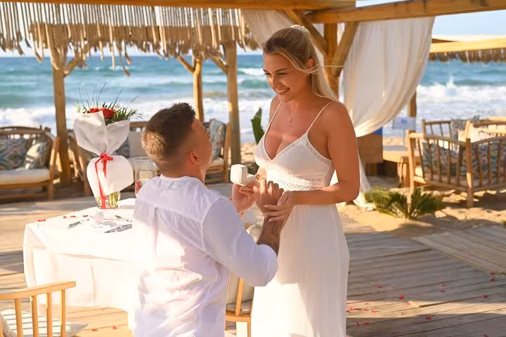 Romantic beach proposal in Hersonissos with man kneeling and woman joyfully accepting under a decorated gazebo.