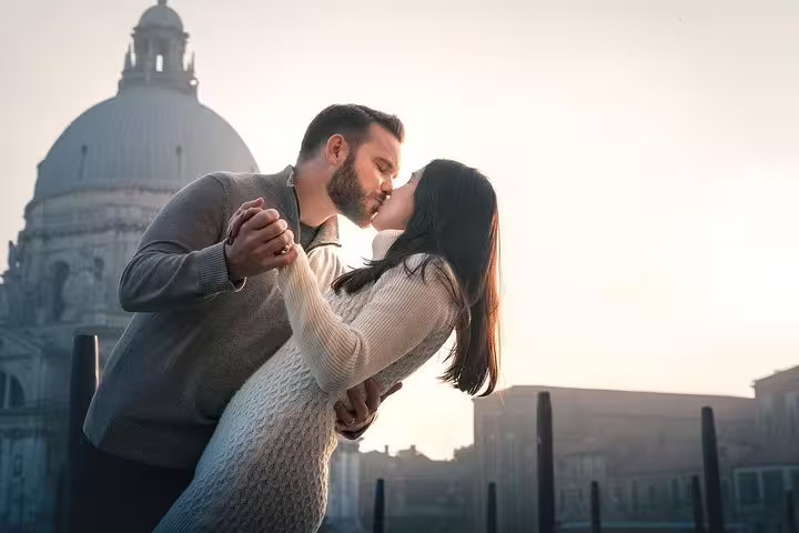 Romantic couple sharing a kiss during a gondola ride with the iconic St. Mark's Basilica in the background.