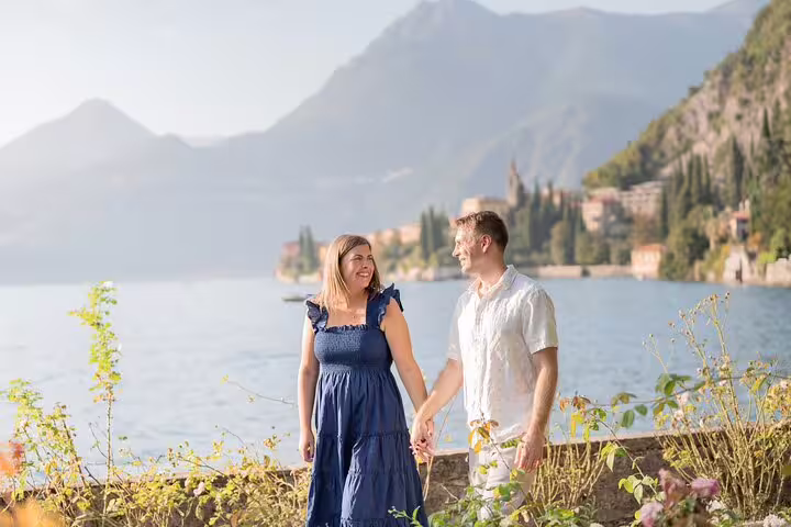 Romantic couple holding hands on Lake Como promenade with mountain views, private travel photo shoot