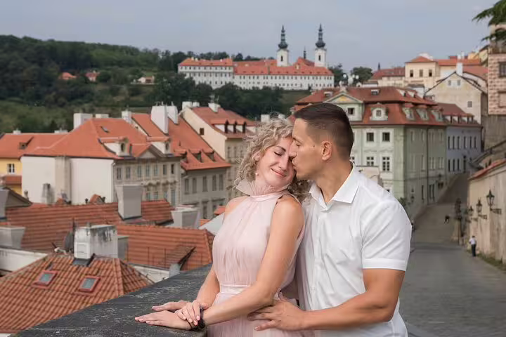 Romantic couple embraces on a scenic terrace overlooking Prague's charming rooftops and historic architecture.
