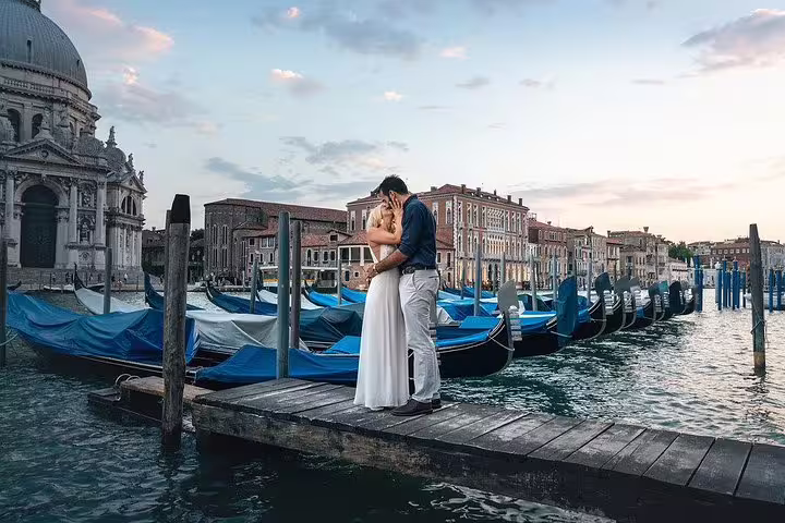 Romantic couple embracing on a Venetian dock with gondolas and historic architecture in the background at sunset.