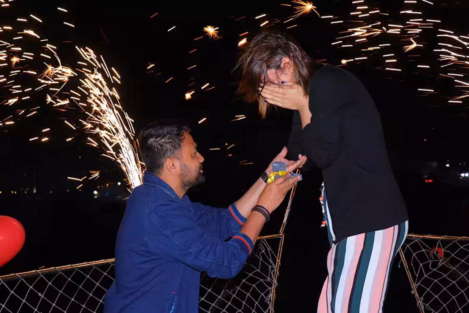 Surprise marriage proposal on a night yacht cruise with sparklers as he presents the ring box to her