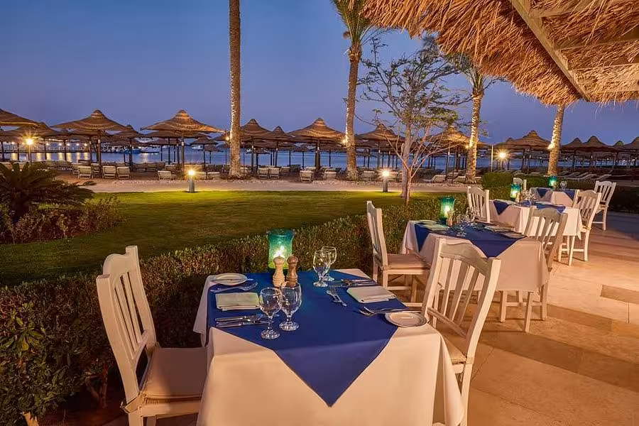 Romantic beachside dining setup at sunset in a Hurghada resort, featuring ocean views and elegant table settings.