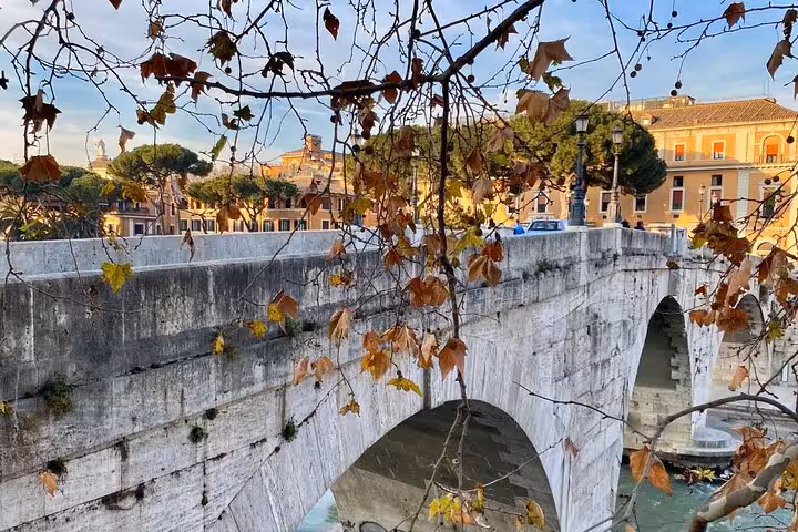 Scenic view of Rome's ancient stone bridge framed by autumn leaves on a Vespa tour.