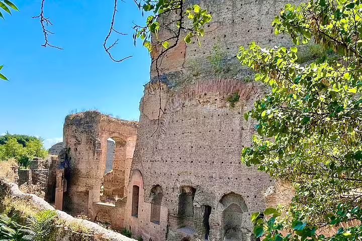 Ancient Roman ruins surrounded by greenery under a bright blue sky on a private Rome sightseeing and catacombs tour