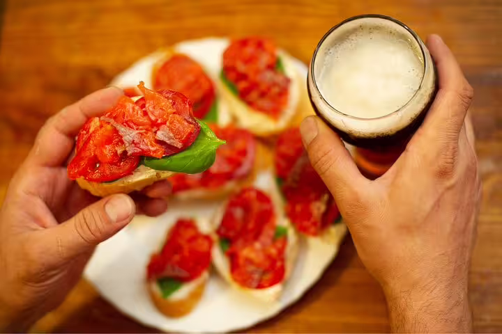Hands holding Italian bruschetta and a frothy drink, showcasing authentic aperitivo experience on a Vatican view tour.