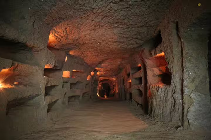Dimly lit ancient corridor of the Rome catacombs on a guided underground group tour with private transfer included