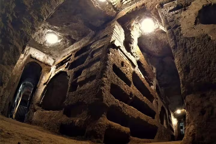 Ancient illuminated burial tunnels in the Rome catacombs visited on a guided underground sightseeing group tour with transfer