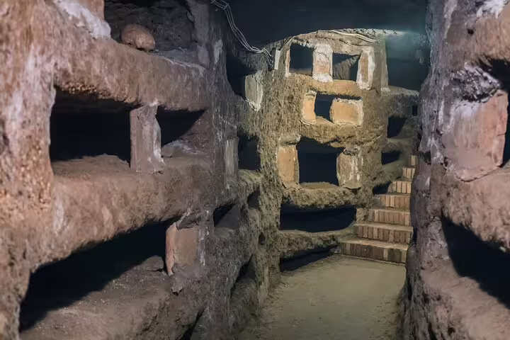Narrow passage and burial niches inside Rome’s historic catacombs explored on a small-group underground tour with hotel transfer