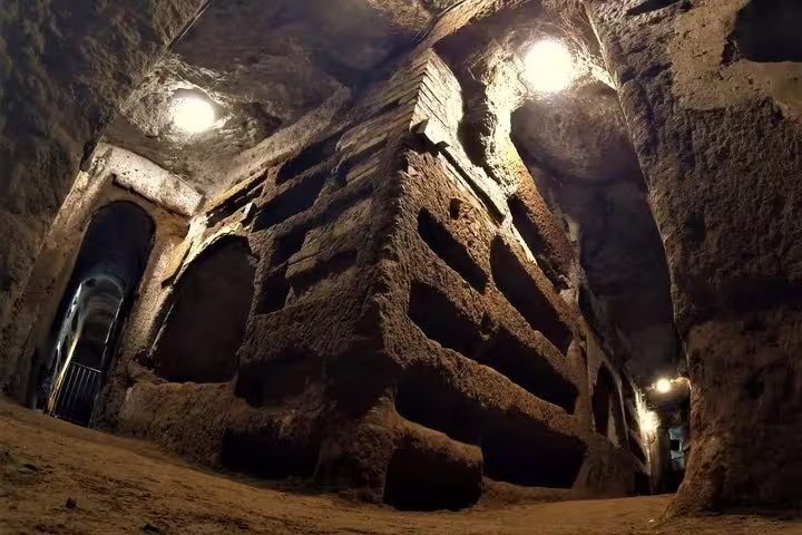 Dimly lit underground passage and stacked tombs in Rome’s early Christian catacombs on a guided small group tour