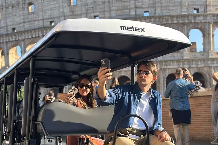 Tourists taking selfies in a golf cart at the Colosseum, enjoying a guided Rome highlights tour.