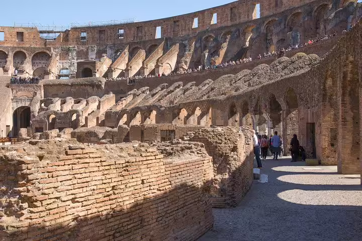 Tour group walking among ancient brick walls inside the Colosseum on a Rome hop on hop off bus and fast track tour
