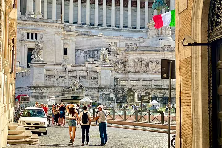 Travelers on a private walking tour stroll past the Vittoriano monument in Rome, near the Colosseum, squares and fountains