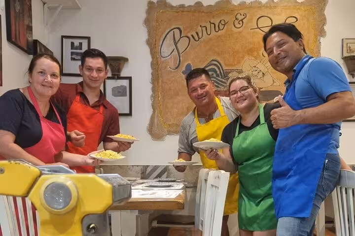 Group of people in colorful aprons proudly display their handmade pasta creations at a cooking class in Rome.