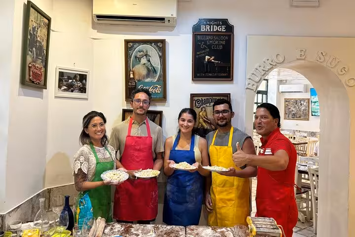 Participants wearing colorful aprons display homemade pasta dishes at a cooking class in Rome.