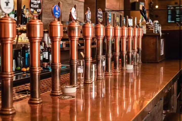 Row of copper beer taps at a cozy bar, highlighting the Vatican's Craft Beer Private Tour with a Local Foodie experience.