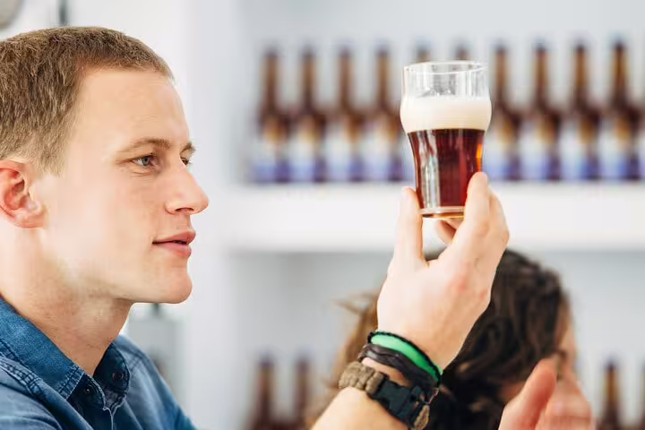 Man examining craft beer in a glass during Vatican's craft beer tour with local foodie, surrounded by beer bottles.