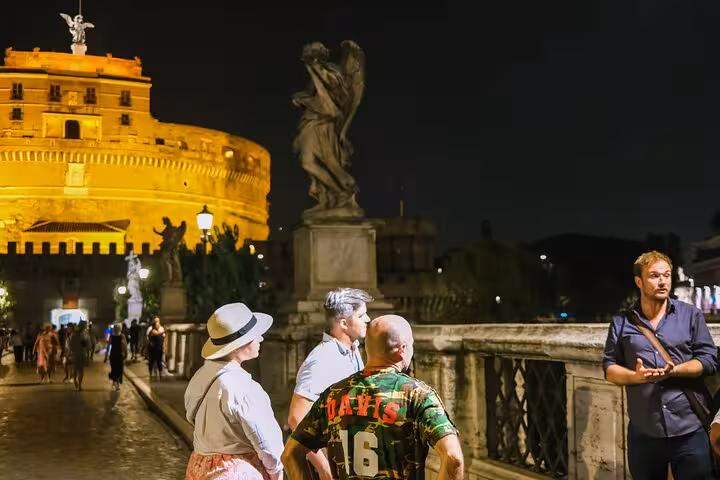 Group listens to guide on Rome's bridge during the Dark Side Tour, with Castel Sant'Angelo lit up at night.