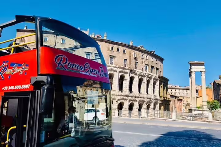 Red Rome open top double decker bus passes ancient ruins on a panoramic guided city sightseeing tour in the historic center