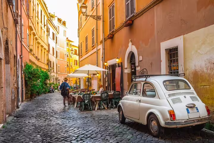 Charming cobblestone street in Rome with vintage car, outdoor cafe, and warm sunset glow, perfect for family-friendly tours.