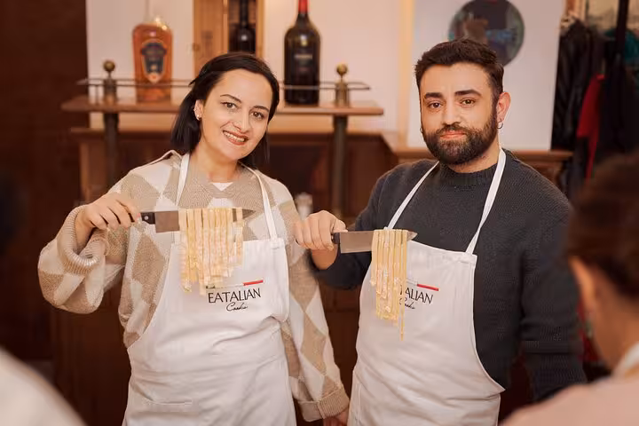 Two proud participants display freshly made Fettuccine at a Rome pasta cooking class, enhancing Italian culinary skills.
