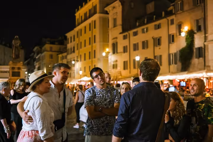 Tour group exploring Rome's eerie legends during a night walk in a lively piazza, part of the ghostly city tour.