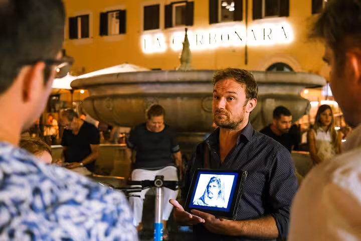 Tour guide shows ghostly image to group at Rome's piazza, highlighting eerie tales on the Dark Side Ghosts Tour.
