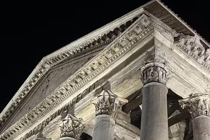 Illuminated ancient Roman temple columns at night on a golf cart tour of Rome with free pick-up service.