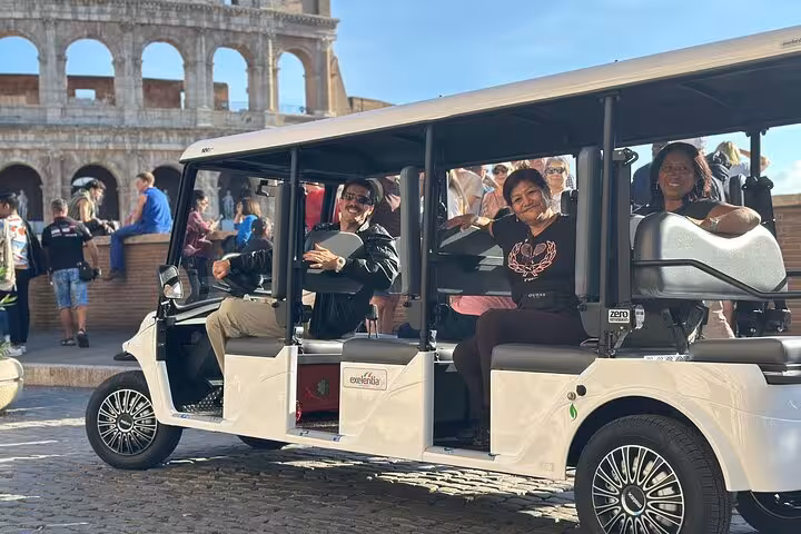 Tourists enjoy a Rome golf cart tour, passing by the iconic Colosseum with a local guide.