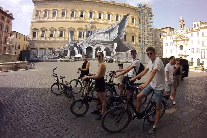 Cyclists pause in front of a grand Roman building, showcasing the charm of Rome's architecture on an e-bike tour.