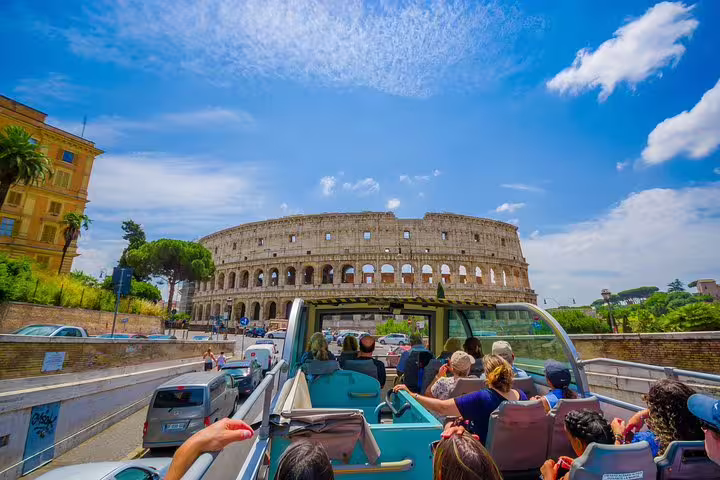 Open top hop on hop off tour bus approaching the Colosseum in Rome on a sunny day with visitors enjoying guided sightseeing
