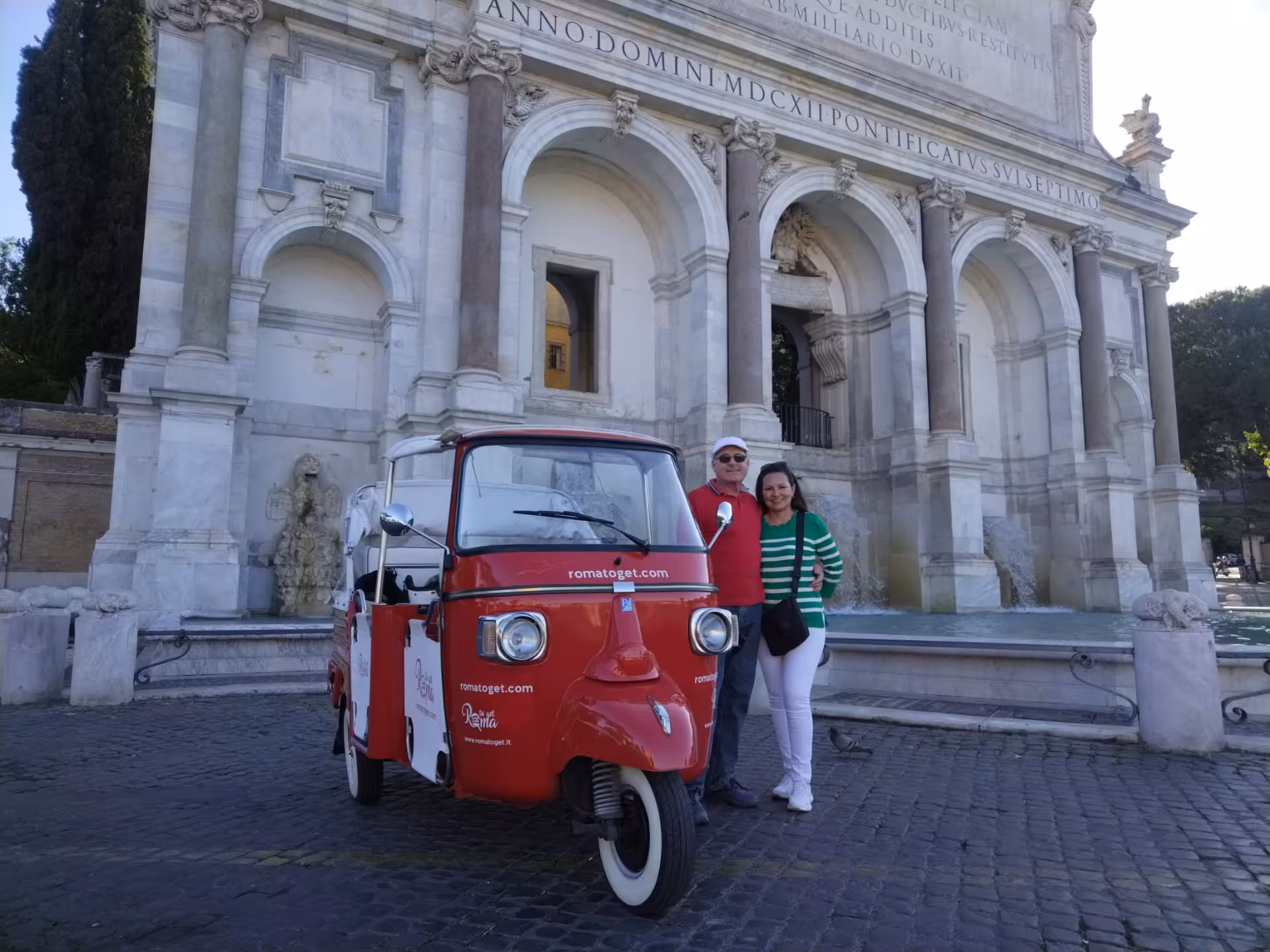 Tourists pose with red tuk tuk at historic fountain during Rome by Night adventure.