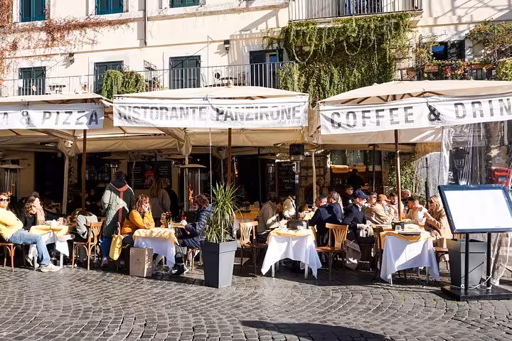 Outdoor cafe in Rome's city center bustling with people enjoying al fresco dining under sunny skies.