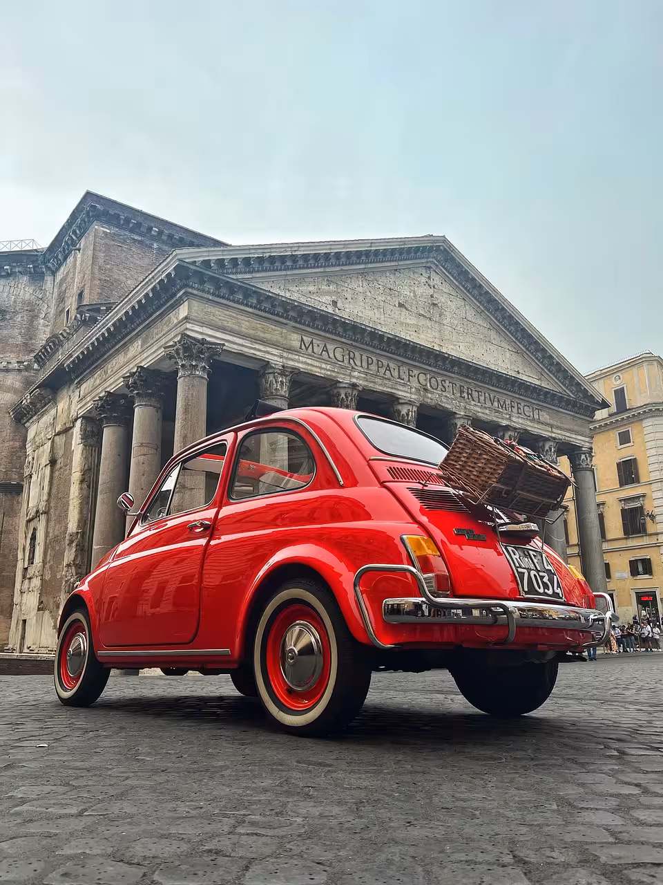 Classic red car with a picnic basket parked in front of Rome's historic Pantheon, showcasing its grand architecture.