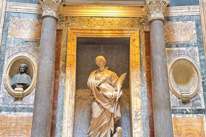 Statue and bust inside Rome's Pantheon, showcasing detailed classical art and ancient Roman architectural beauty.