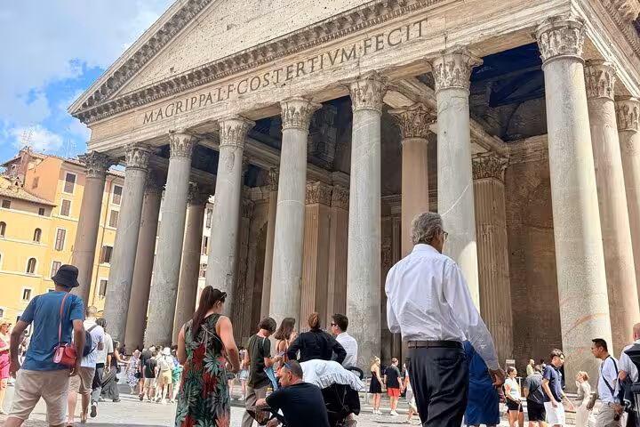 Tourists gather outside the ancient Roman Pantheon, showcasing its iconic columns and historic inscriptions under a clear sky.