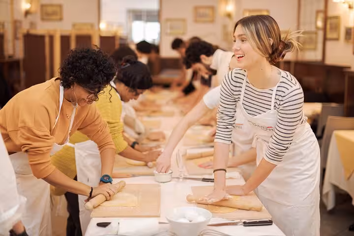Participants in a Rome pasta class roll out fresh fettuccine dough in a lively Piazza Navona setting.