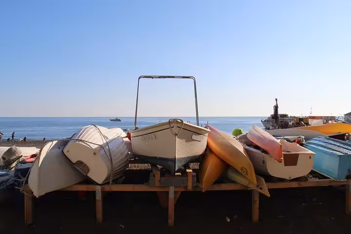 Rowboats and kayaks lined up on a beach with a serene view of the Mediterranean Sea in the background.