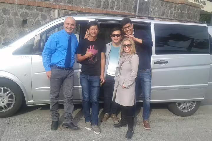 Happy small group with chauffeur beside modern minivan after private Rome to Positano transfer along the Amalfi Coast