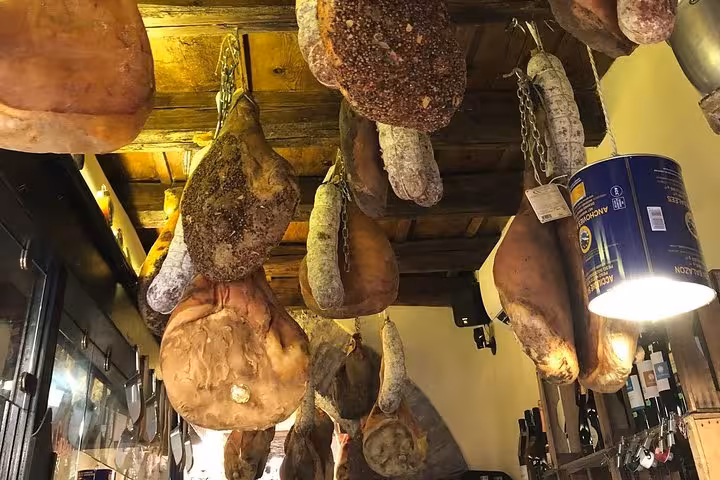Cured meats and hams hang in an Italian deli, a highlight of the Rome Rione Parione walking food tour.