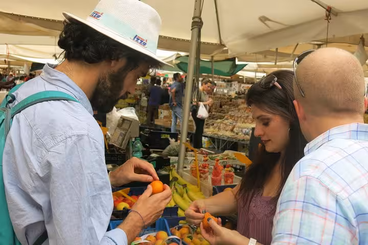 Tourists exploring fresh produce at a vibrant market in Rome's Rione Parione district.
