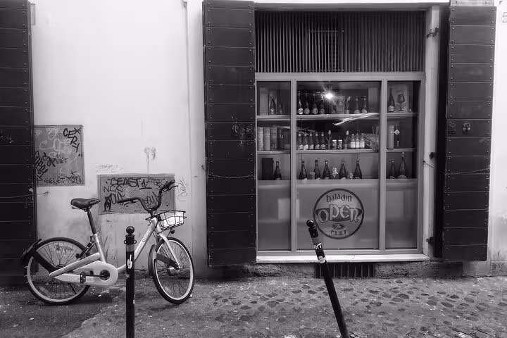 Black and white image of a Rome street with a bicycle and a storefront displaying craft beers for the Art & Craft Beer Tour.