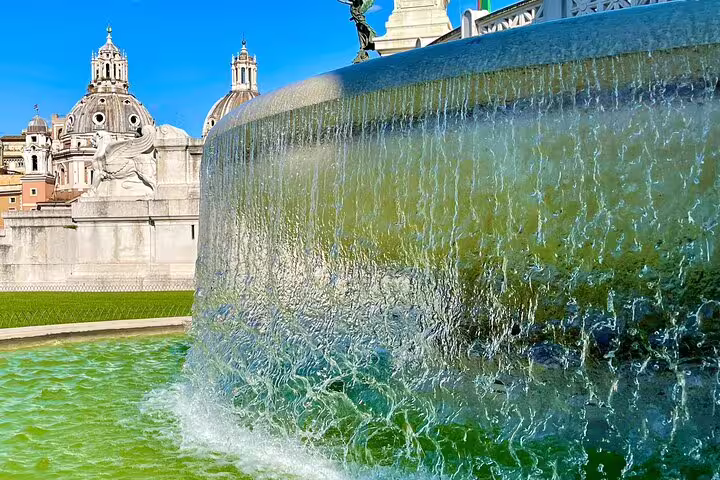 Cascading fountain at Piazza Venezia with domes of Rome churches on exclusive Civitavecchia to Vatican City day tour