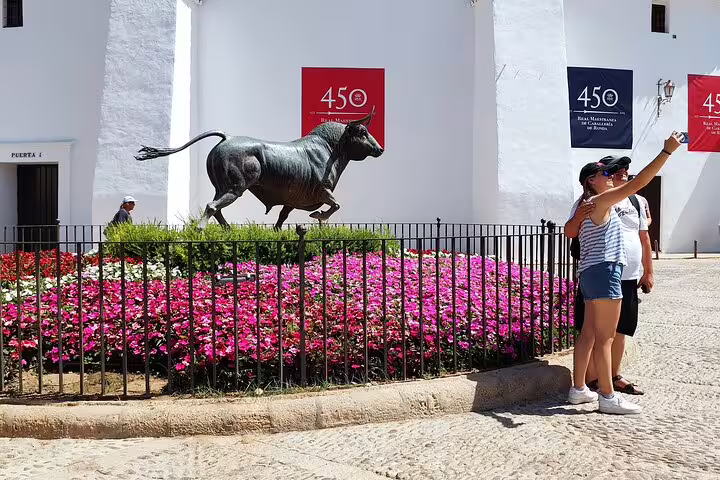 Visitors take a selfie near the iconic bull statue and vibrant flowers at the historic Ronda Bullring.