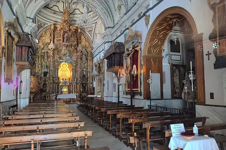 Ornate interior of a historic church in Ronda, featuring intricate wood carvings and a glowing altar centerpiece.
