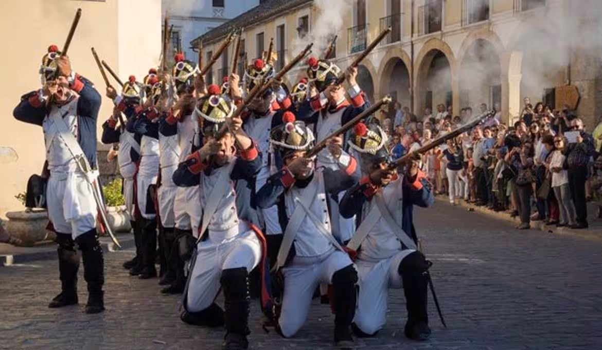 Historical reenactors in traditional military costumes perform in Ronda's vibrant street festival, captivating onlookers.