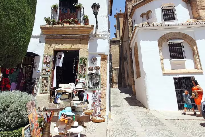 Bustling street in Ronda with a quaint shop displaying hats and souvenirs, ideal for a private walking tour.