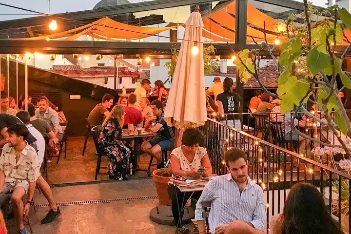 People enjoying vibrant evening at a rooftop bar in Madrid, surrounded by warm lights and lively atmosphere, perfect for a bar crawl experience.