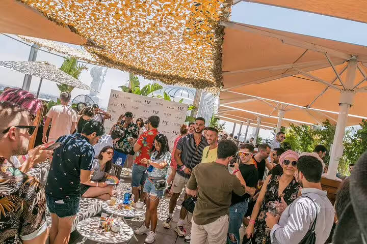 Guests enjoying a lively rooftop bar crawl in Madrid, surrounded by vibrant decor and panoramic city views under sunny skies.