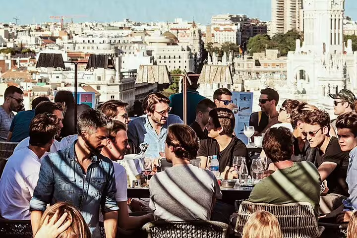 People enjoying drinks and conversation at a vibrant rooftop bar with stunning views of Madrid's cityscape on a sunny day.
